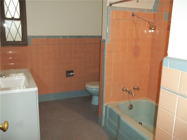 full bathroom with tile walls, tiled shower / bath, vanity, and toilet