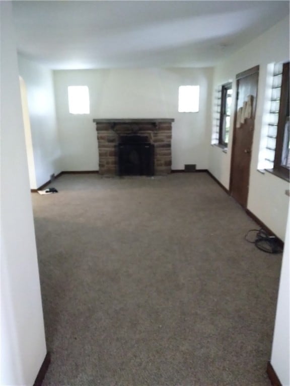 unfurnished living room with a stone fireplace and carpet flooring