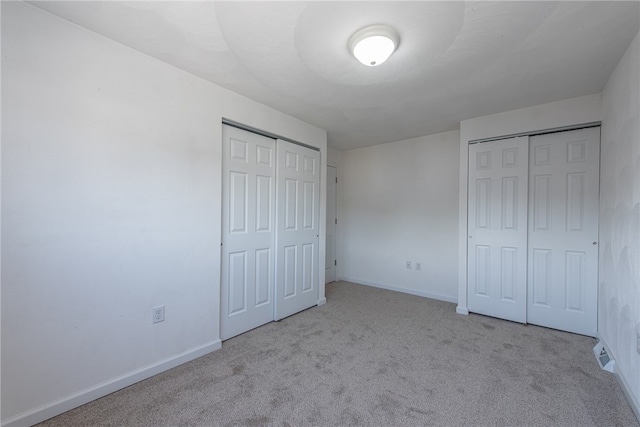 unfurnished bedroom with light carpet and two closets