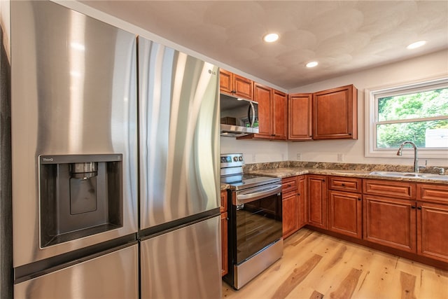 kitchen with light wood-type flooring, appliances with stainless steel finishes, light stone countertops, and sink