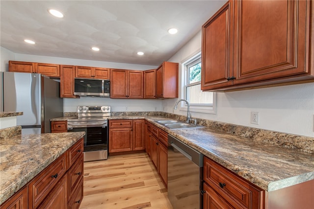 kitchen with light wood-type flooring, appliances with stainless steel finishes, sink, and dark stone counters