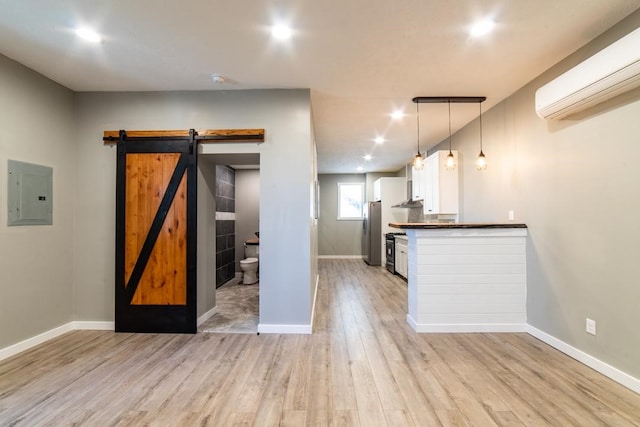 kitchen featuring a wall mounted air conditioner, hanging light fixtures, stainless steel fridge, a barn door, and light wood-type flooring