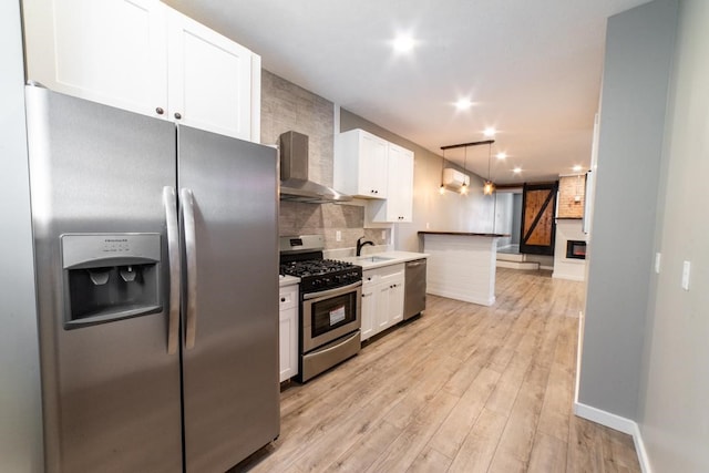 kitchen featuring appliances with stainless steel finishes, white cabinetry, light hardwood / wood-style floors, and wall chimney range hood