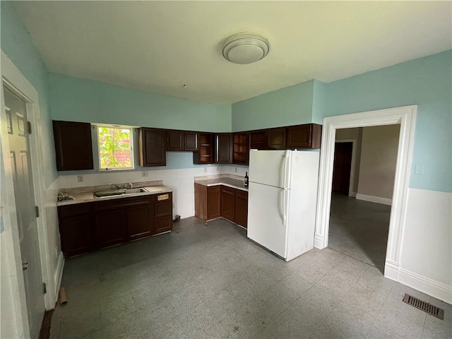 kitchen featuring dark brown cabinetry, sink, white fridge, and light tile floors