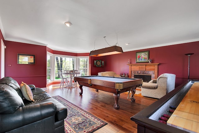 playroom with pool table, ornamental molding, wood-type flooring, and a brick fireplace