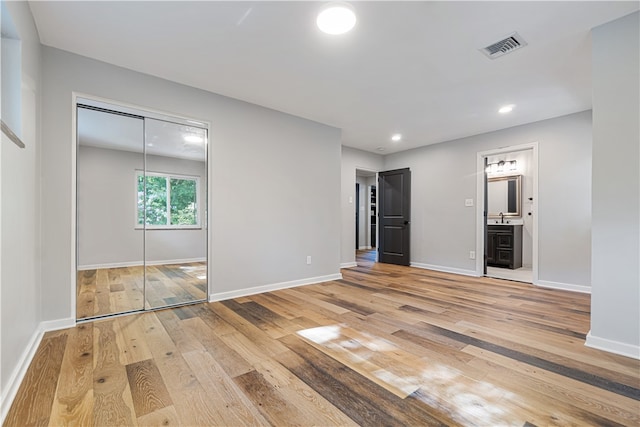 unfurnished bedroom featuring a closet, light hardwood / wood-style floors, ensuite bath, and sink