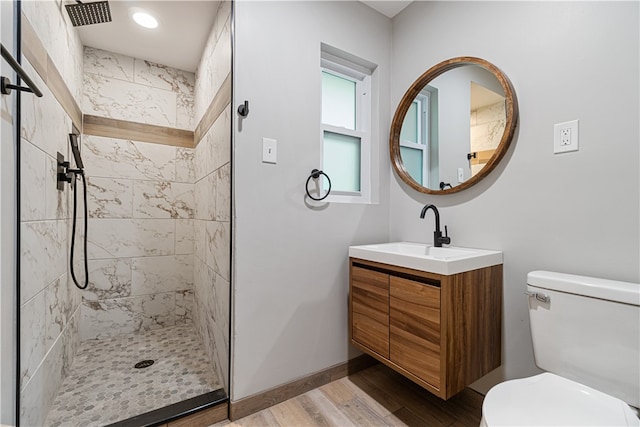 bathroom featuring a tile shower, wood-type flooring, vanity, and toilet