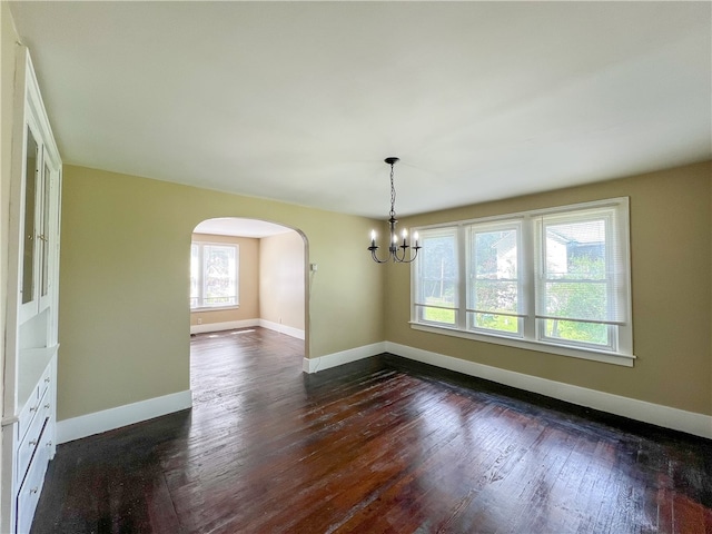 unfurnished room with a healthy amount of sunlight, dark hardwood / wood-style flooring, and an inviting chandelier