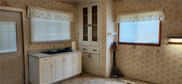 kitchen with a healthy amount of sunlight, sink, white cabinetry, and light tile floors