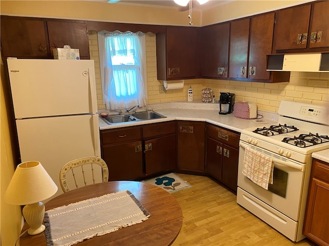 kitchen featuring wall chimney range hood, dark brown cabinetry, light hardwood / wood-style floors, sink, and white appliances