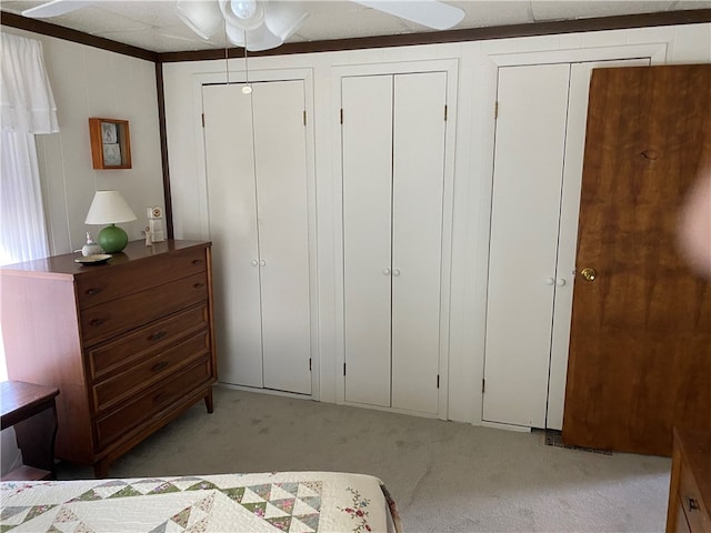 bedroom featuring two closets, ceiling fan, and light colored carpet