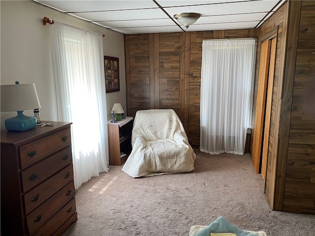 bedroom with carpet flooring, wood walls, and multiple windows