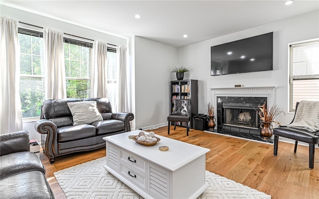 living room with a high end fireplace, a healthy amount of sunlight, and light wood-type flooring