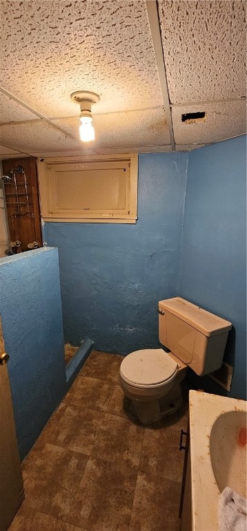 bathroom featuring tile floors, vanity, toilet, and a drop ceiling