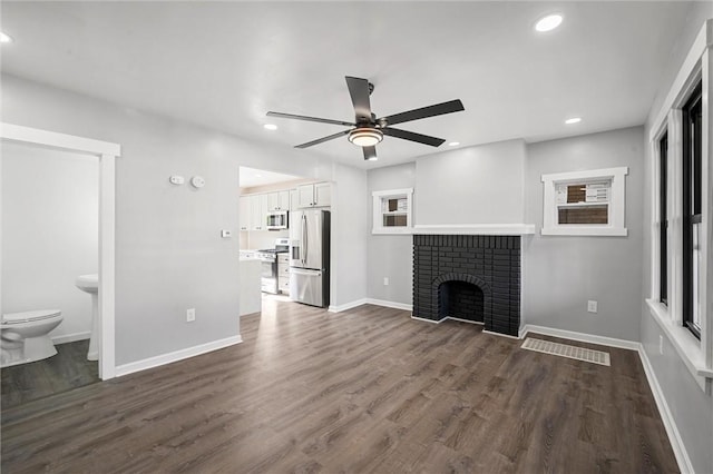 unfurnished living room with ceiling fan, a brick fireplace, and dark hardwood / wood-style flooring