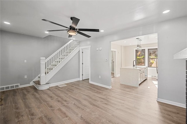 unfurnished living room featuring ceiling fan, sink, and light wood-type flooring