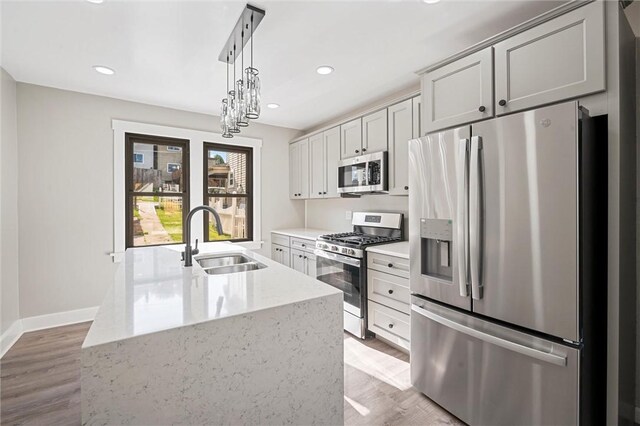 kitchen with stainless steel appliances, pendant lighting, light stone countertops, sink, and light hardwood / wood-style floors