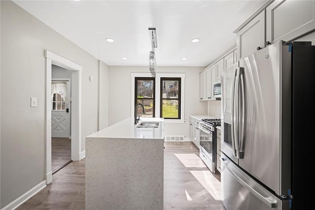 kitchen with appliances with stainless steel finishes, a kitchen island with sink, light hardwood / wood-style floors, sink, and decorative light fixtures