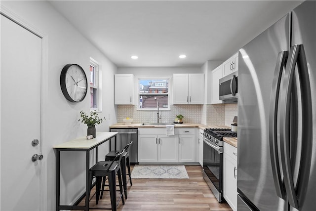 kitchen with sink, decorative backsplash, light wood-type flooring, white cabinetry, and stainless steel appliances