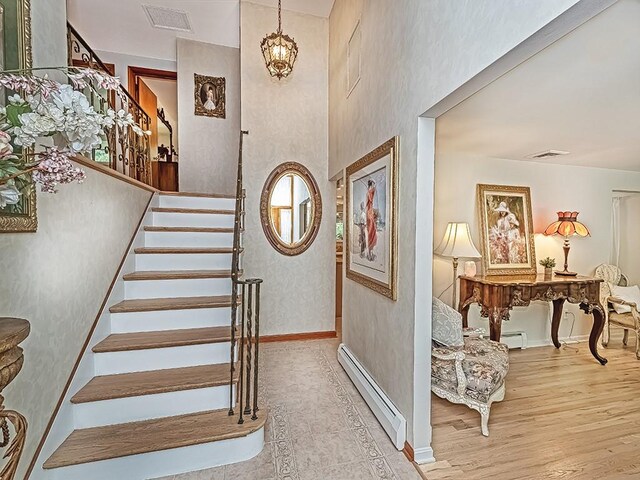 stairway with a baseboard heating unit, hardwood / wood-style flooring, and an inviting chandelier