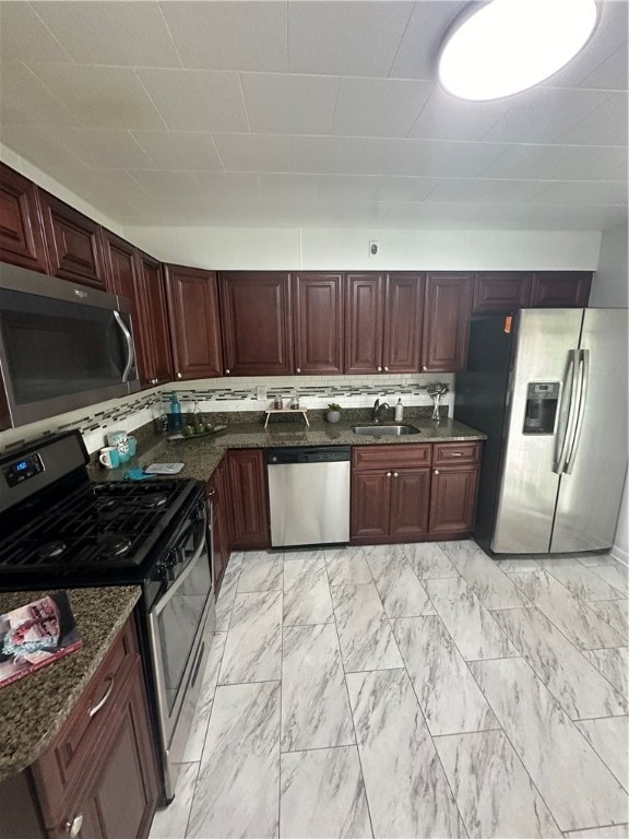 kitchen featuring stainless steel appliances, dark stone counters, backsplash, sink, and light tile floors