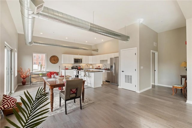 dining space with sink, a towering ceiling, and light hardwood / wood-style flooring