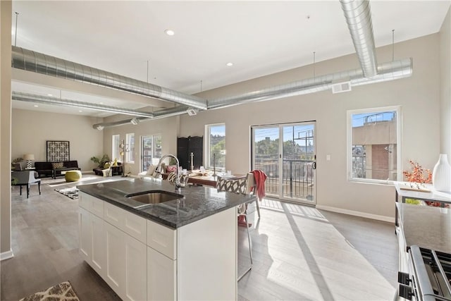 kitchen with sink, white cabinets, dark stone counters, a center island with sink, and light hardwood / wood-style flooring