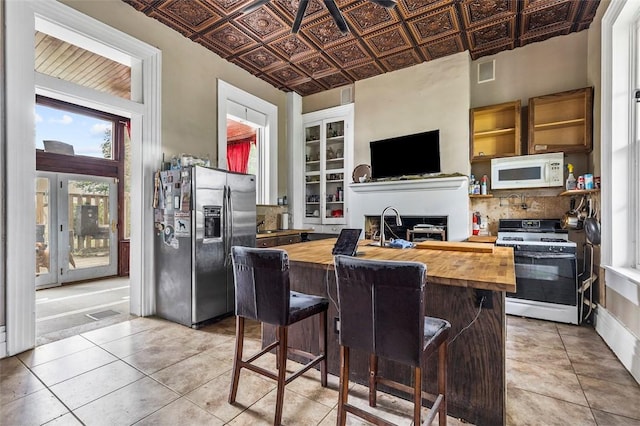 kitchen with a kitchen bar, light tile patterned floors, white appliances, and wood counters