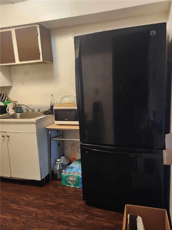 kitchen featuring black refrigerator, sink, white cabinetry, and dark wood-type flooring