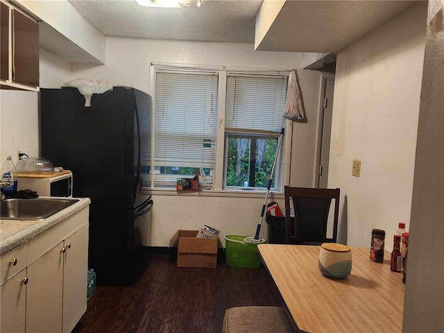 kitchen featuring dark wood-type flooring, black fridge, and sink