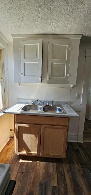 interior space with a textured ceiling, sink, an island with sink, and dark wood-type flooring