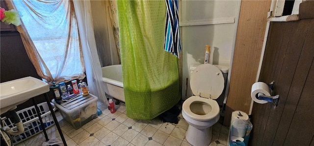 bathroom featuring tile patterned floors, wood walls, shower / tub combo with curtain, and toilet