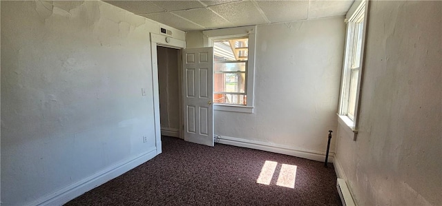 unfurnished room with plenty of natural light, dark carpet, and a drop ceiling