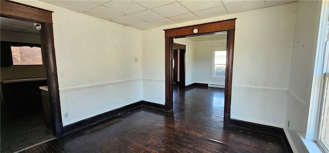 spare room with a drop ceiling, dark wood-type flooring, and a baseboard radiator