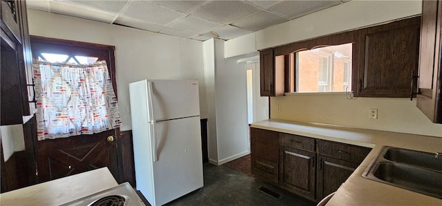 kitchen with dark brown cabinets, white refrigerator, a drop ceiling, and sink