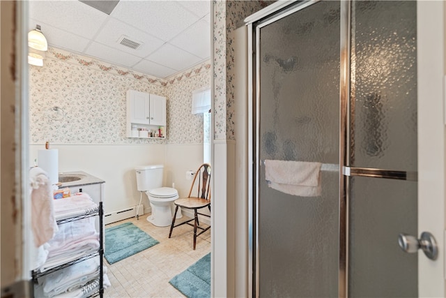 bathroom with a baseboard heating unit, a paneled ceiling, a shower with door, vanity, and toilet