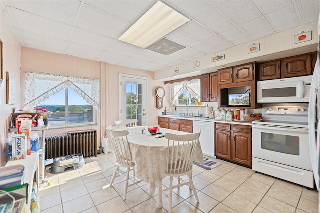 kitchen featuring radiator heating unit, sink, light tile patterned floors, and white appliances