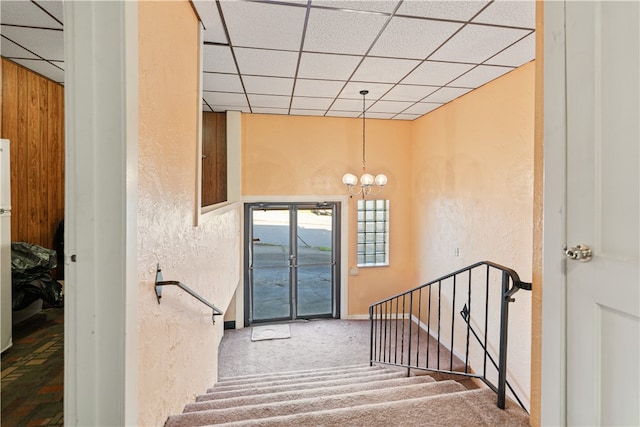 stairway featuring a paneled ceiling, carpet flooring, and an inviting chandelier