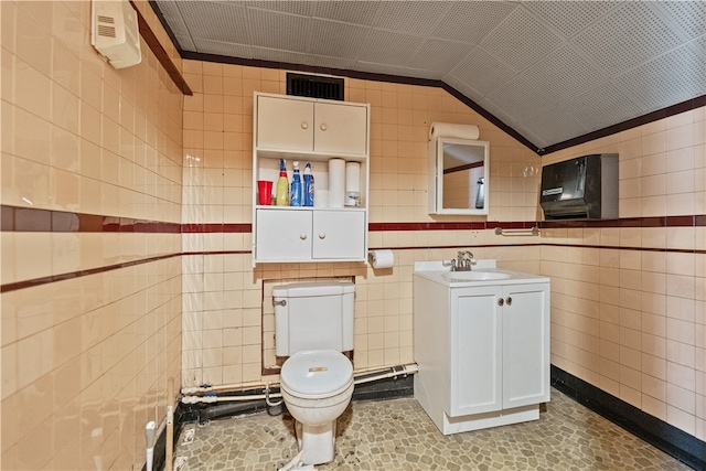 bathroom featuring vanity, lofted ceiling, toilet, and tile walls