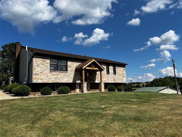 split foyer home with stone siding, a chimney, and a front yard