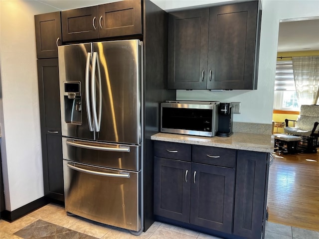 kitchen with light wood-type flooring, light stone counters, dark brown cabinets, and stainless steel refrigerator with ice dispenser