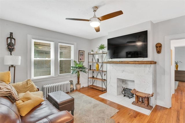 living room featuring a fireplace, light hardwood / wood-style flooring, radiator, and ceiling fan