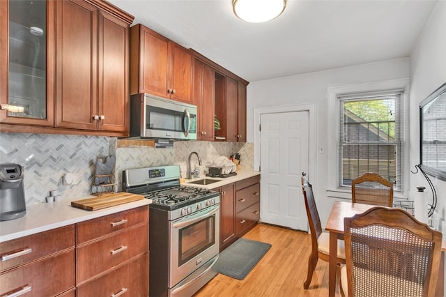 kitchen with backsplash, sink, light hardwood / wood-style floors, and appliances with stainless steel finishes