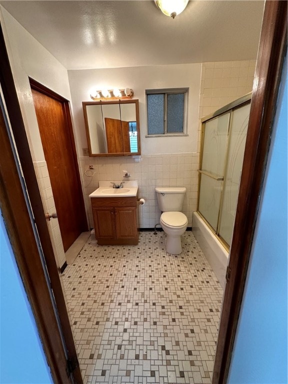 bathroom with tile walls, toilet, tile floors, a shower with shower door, and vanity