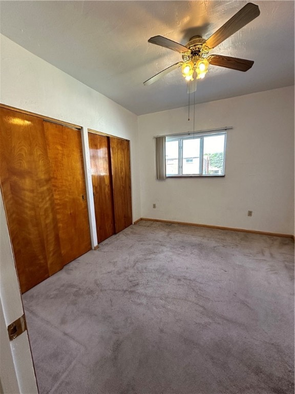 unfurnished bedroom with two closets, ceiling fan, and carpet floors