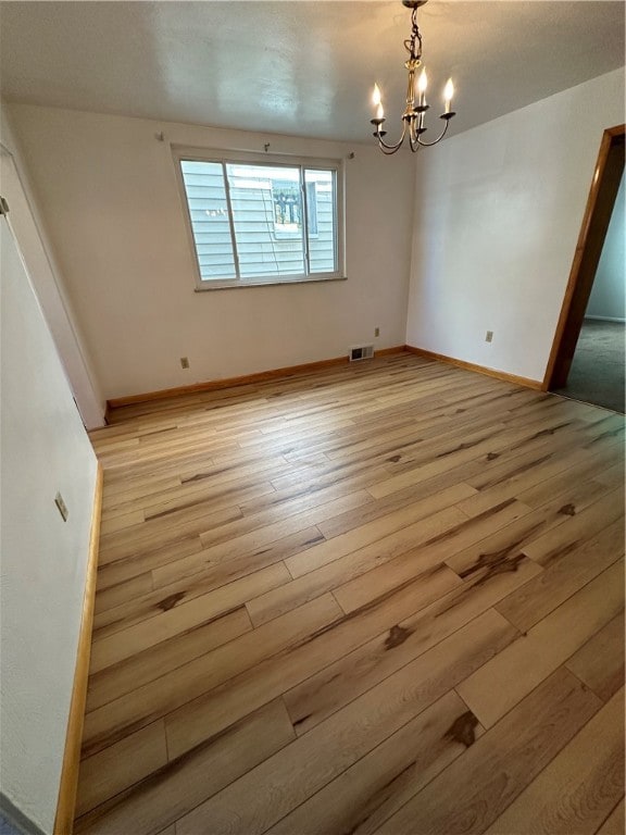 empty room with a notable chandelier and wood-type flooring