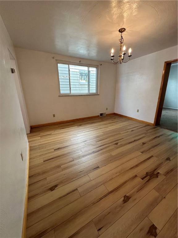 unfurnished room with a notable chandelier and light hardwood / wood-style floors