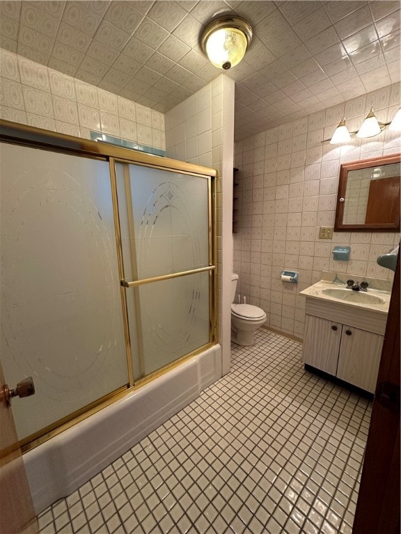 full bathroom with combined bath / shower with glass door, tile walls, toilet, tile floors, and vanity