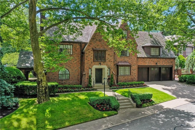 tudor house featuring a garage, concrete driveway, brick siding, and a front lawn