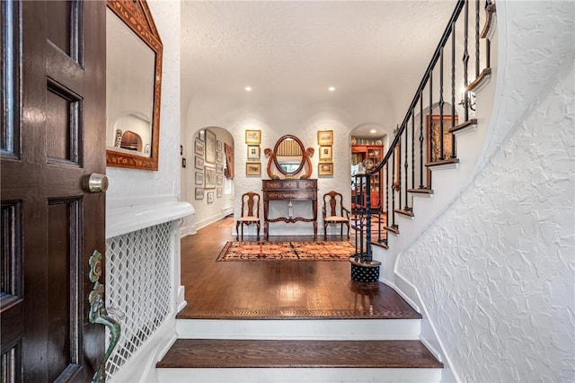 stairs with baseboards, arched walkways, a textured wall, wood finished floors, and a textured ceiling